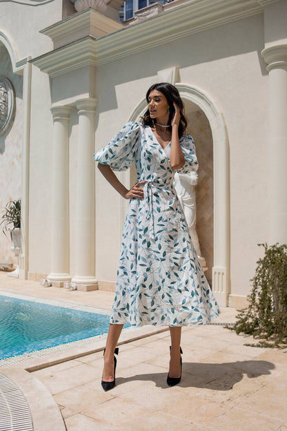 Woman in a floral dress standing by a pool with classical architecture in the background