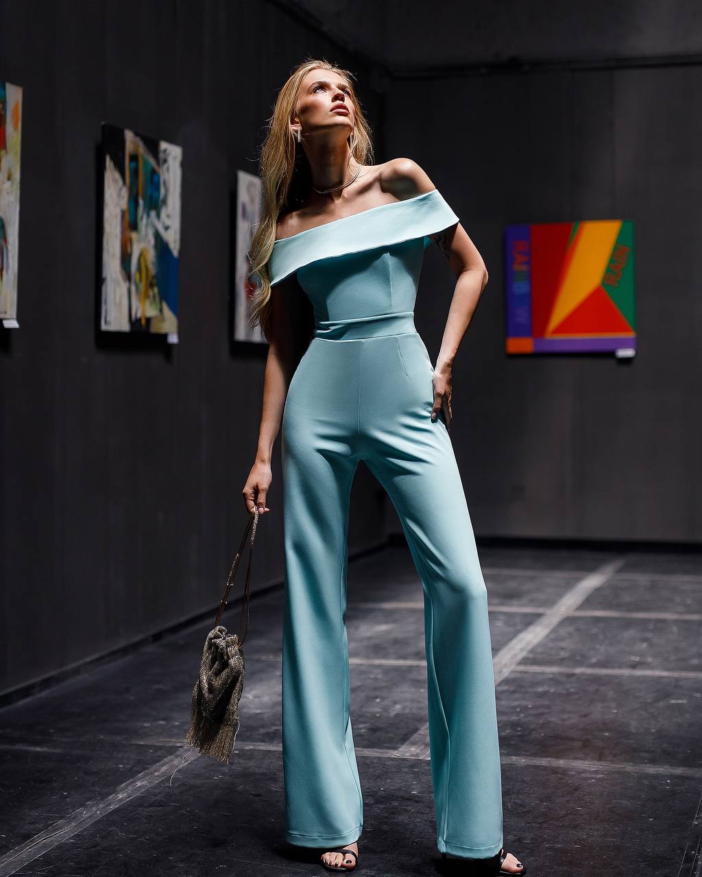 Woman in a light blue off-shoulder jumpsuit standing in an art gallery.