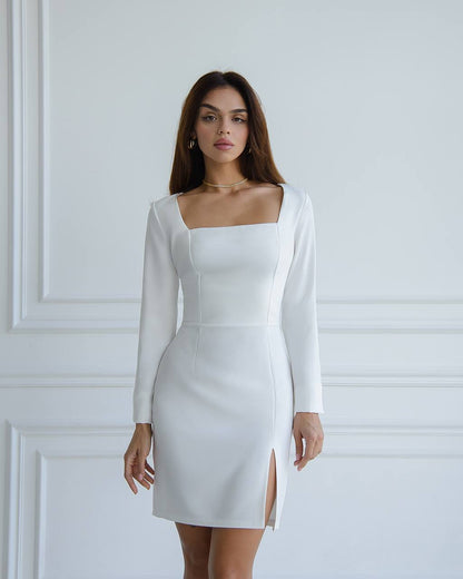 Woman wearing a white dress with long sleeves against a white wall