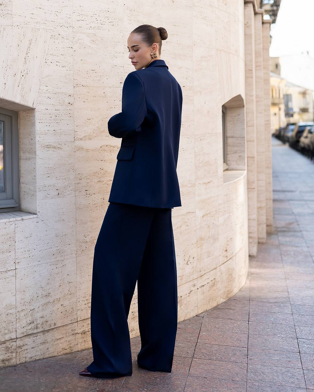 Woman in a navy blue suit standing against a light-colored wall.
