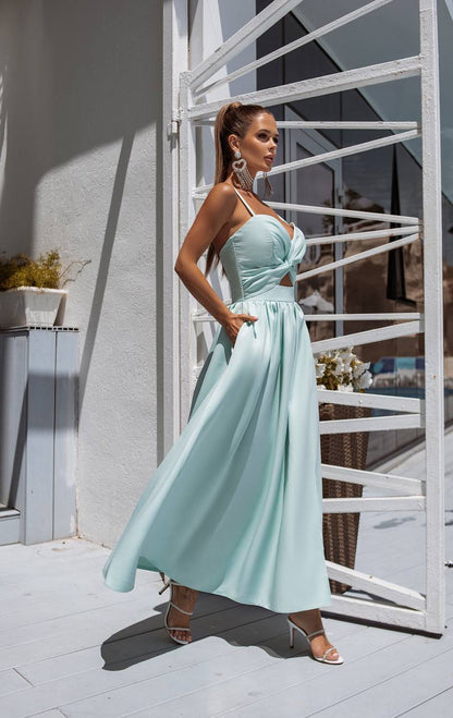 Woman in a light blue dress standing outdoors near a white metal gate.
