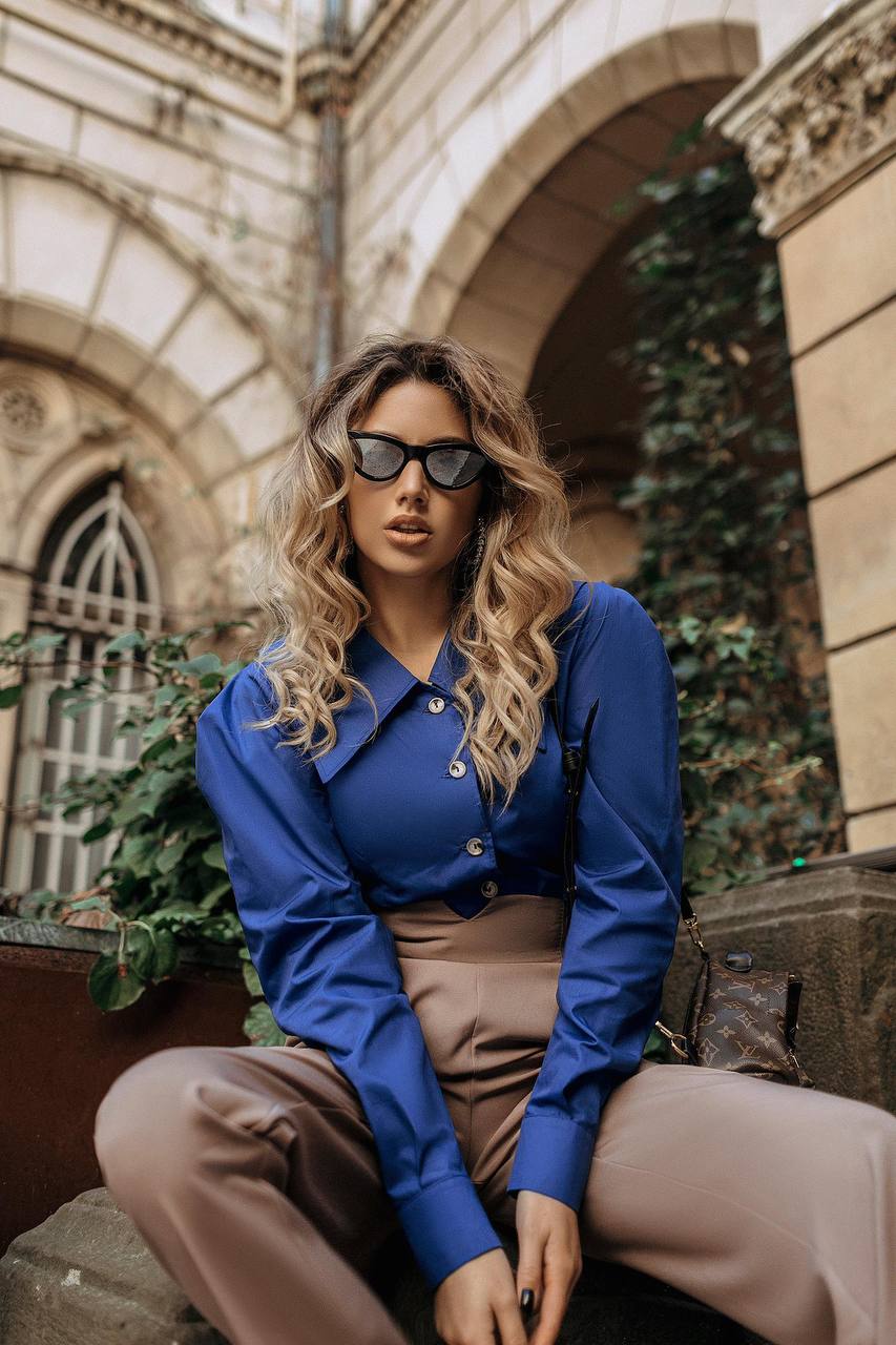 Woman wearing a blue shirt and beige pants sitting outdoors with architectural background