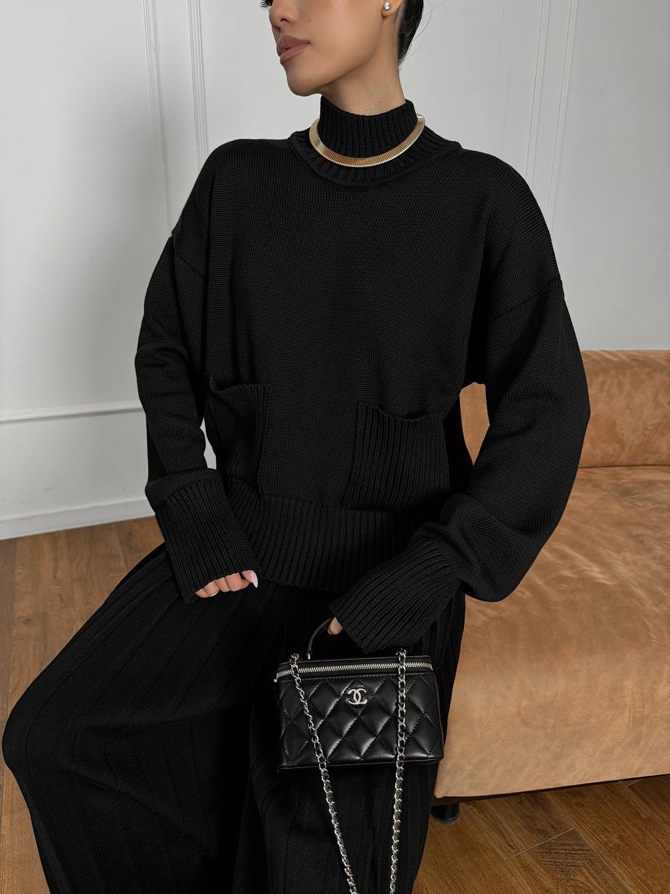 Person wearing a black outfit with a Chanel handbag in a minimal indoor setting