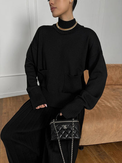 Person wearing a black outfit with a Chanel handbag in a minimal indoor setting