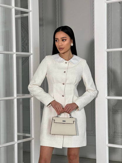 Woman in a white dress holding a beige handbag in front of a glass door.