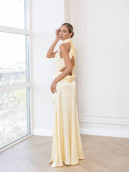 Woman in a light yellow dress standing in a bright room with large windows.