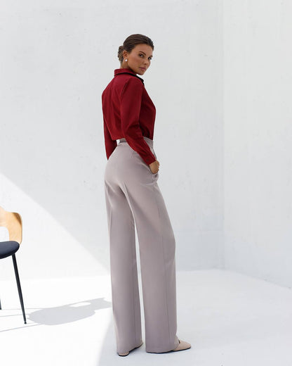 Woman wearing a red blouse and light gray pants on a white background