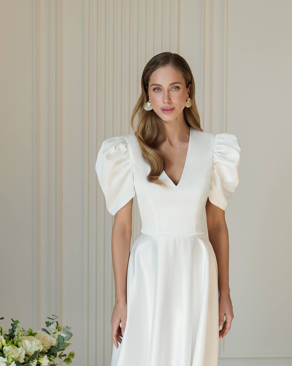 Woman wearing a white wedding dress with puffed sleeves against a neutral background