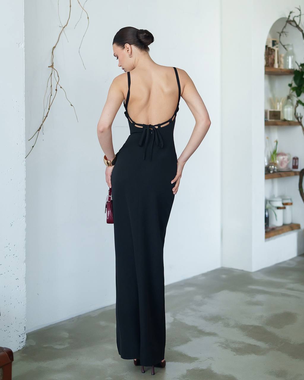 Woman wearing a black open-back jumpsuit in a minimalistic room.