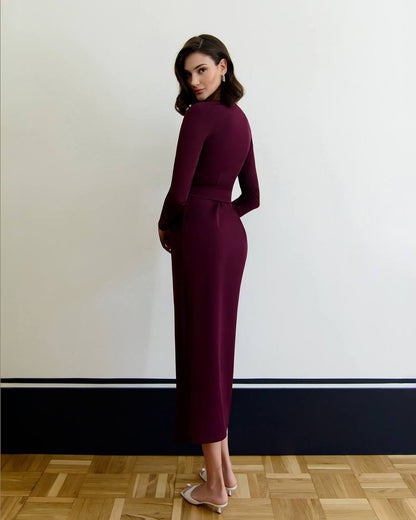 Woman in a burgundy dress standing against a white wall with a wooden floor.