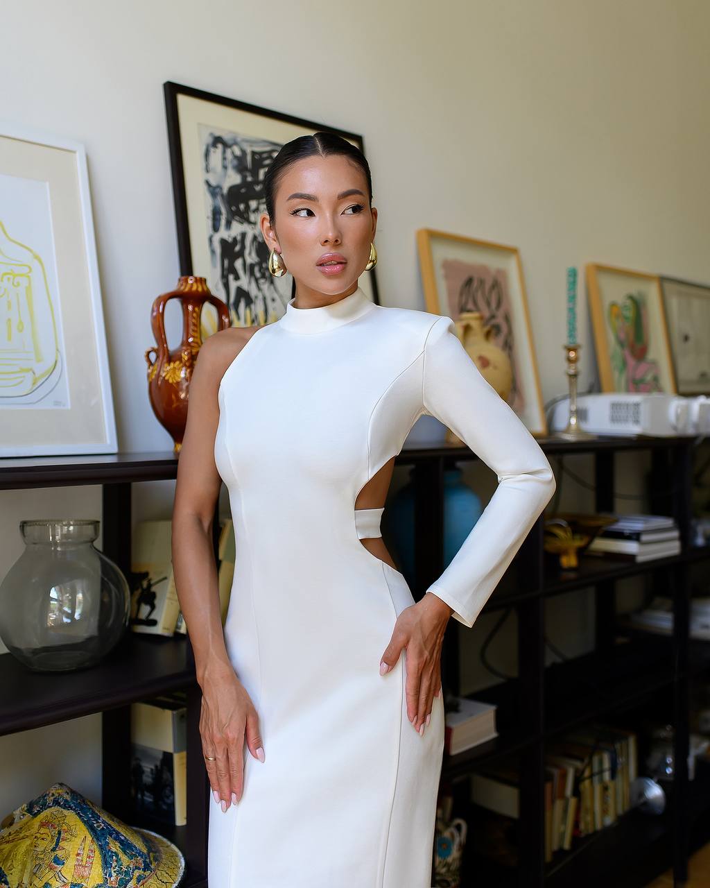 Woman in a white dress standing in a room with shelves and decor