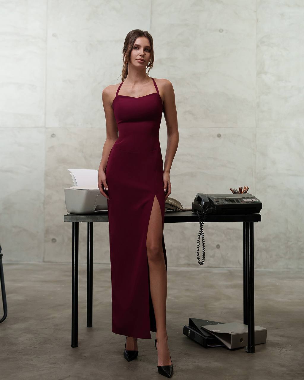 Woman in a burgundy dress standing in an office setting.