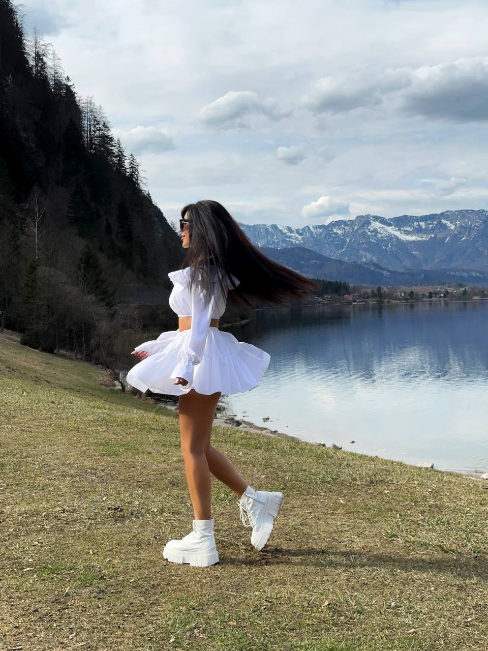 Woman in a white outfit standing by a lake with mountains in the background