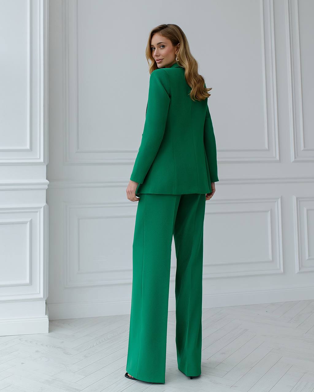 Woman wearing a green suit standing against a white paneled wall.