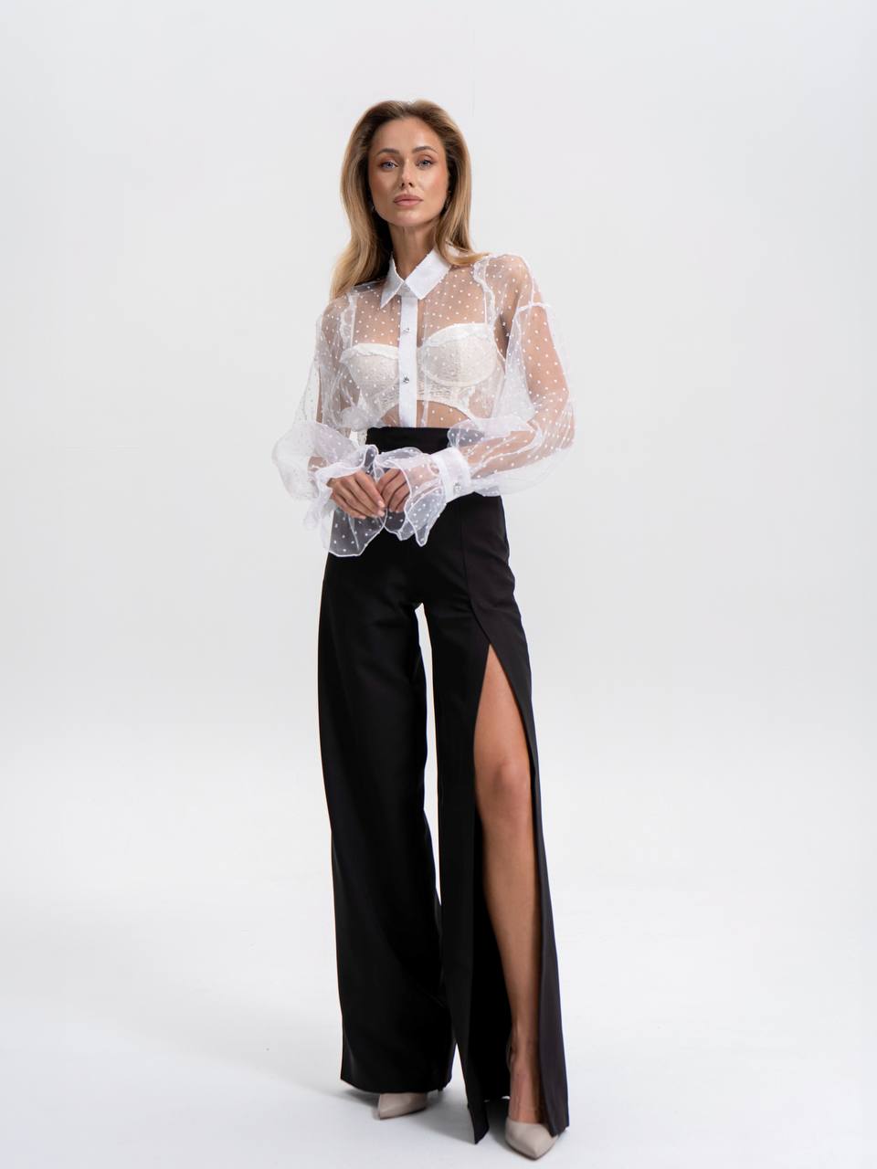 Woman wearing a white sheer blouse with a black high-waisted pants on a white background