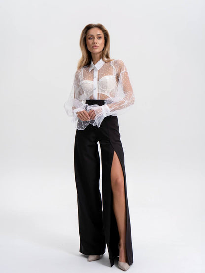 Woman wearing a white sheer blouse with a black high-waisted pants on a white background