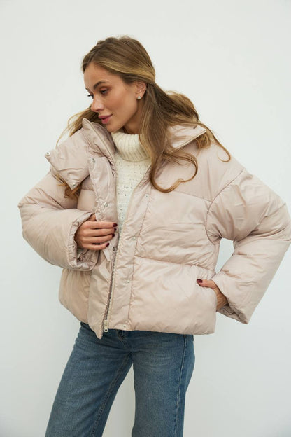 Woman wearing a beige puffer jacket against a white background