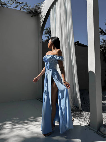 Woman in a light blue off-shoulder dress standing in front of a white curtain.