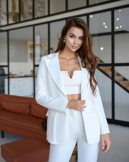 Woman in a white outfit standing in a modern indoor setting with glass walls and brown furniture.