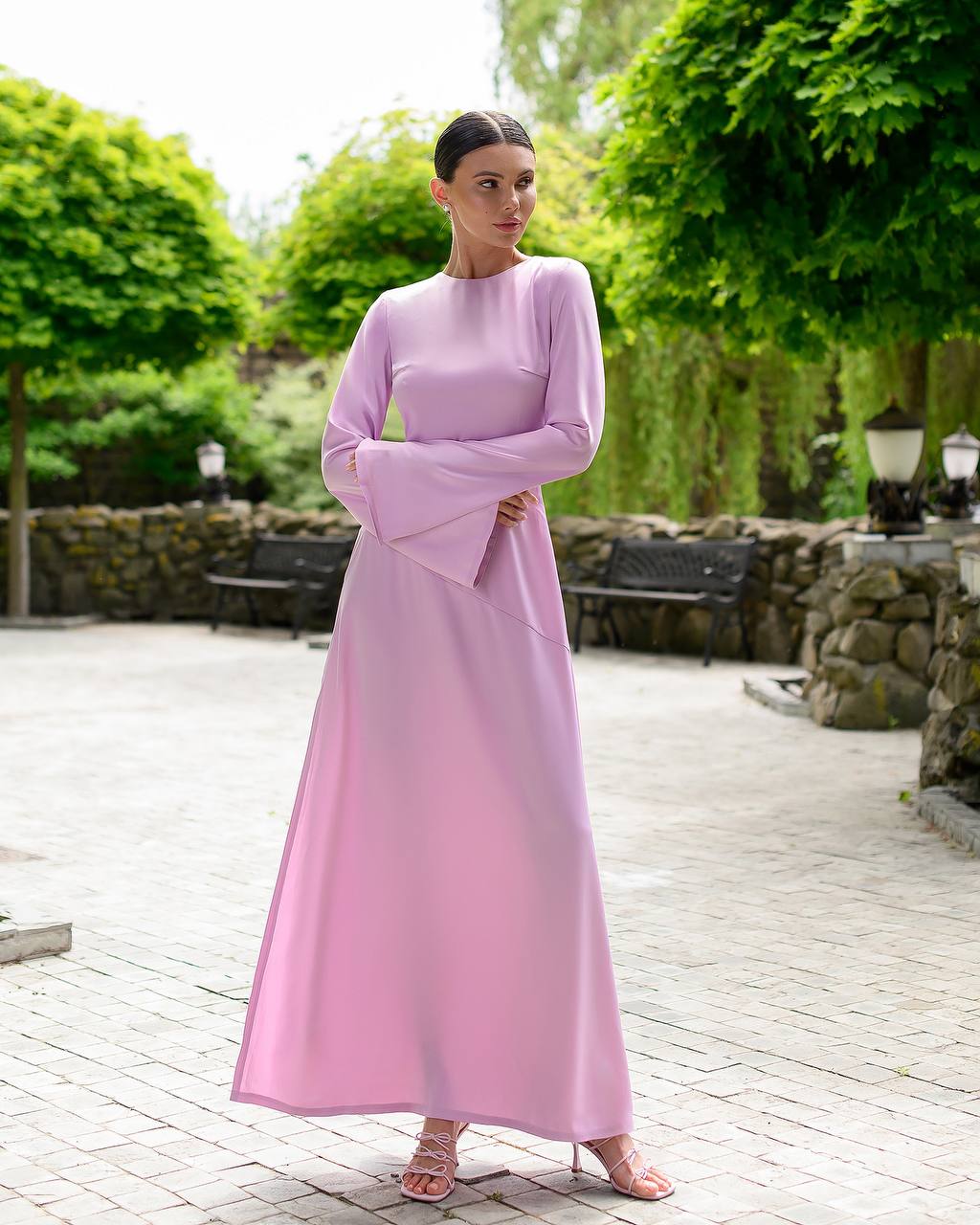 Woman in a pink dress standing in an outdoor setting with greenery.