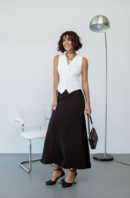 Woman in a white sleeveless top and black skirt standing in a minimalistic room.