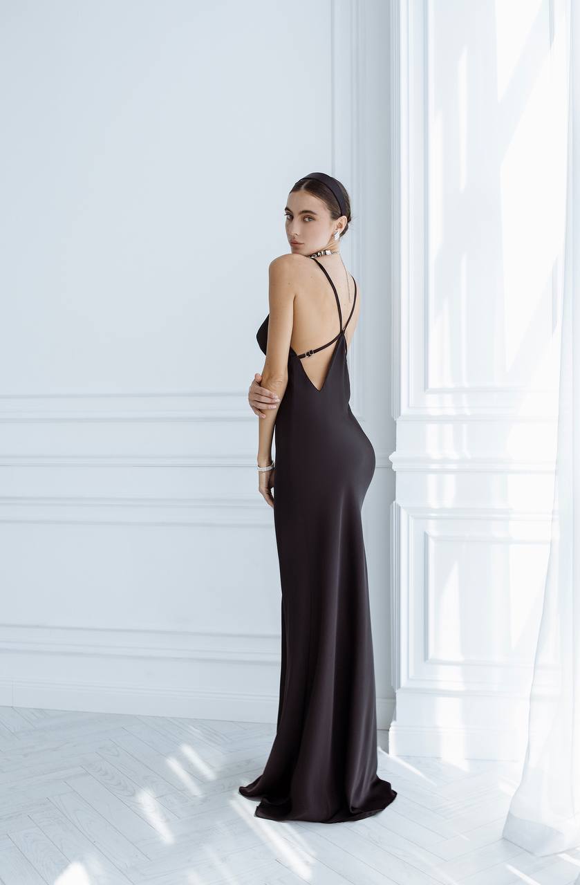 Woman in a black evening gown standing against a white wall.