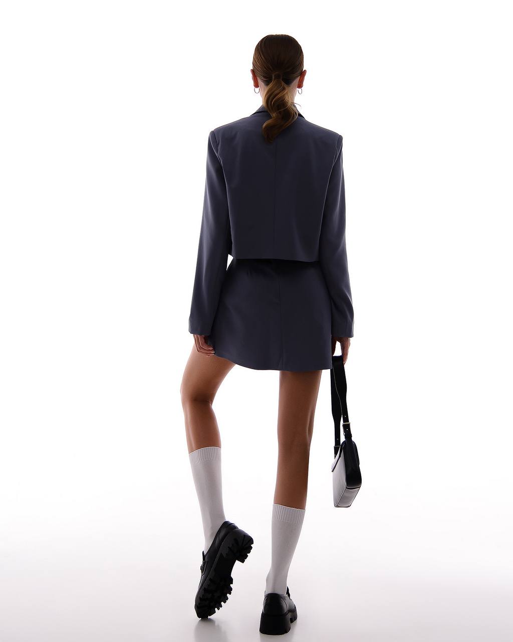 Person wearing a navy blazer and skirt with white socks and black shoes on a white background