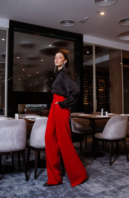 Woman in a black top and red pants standing in a modern restaurant.