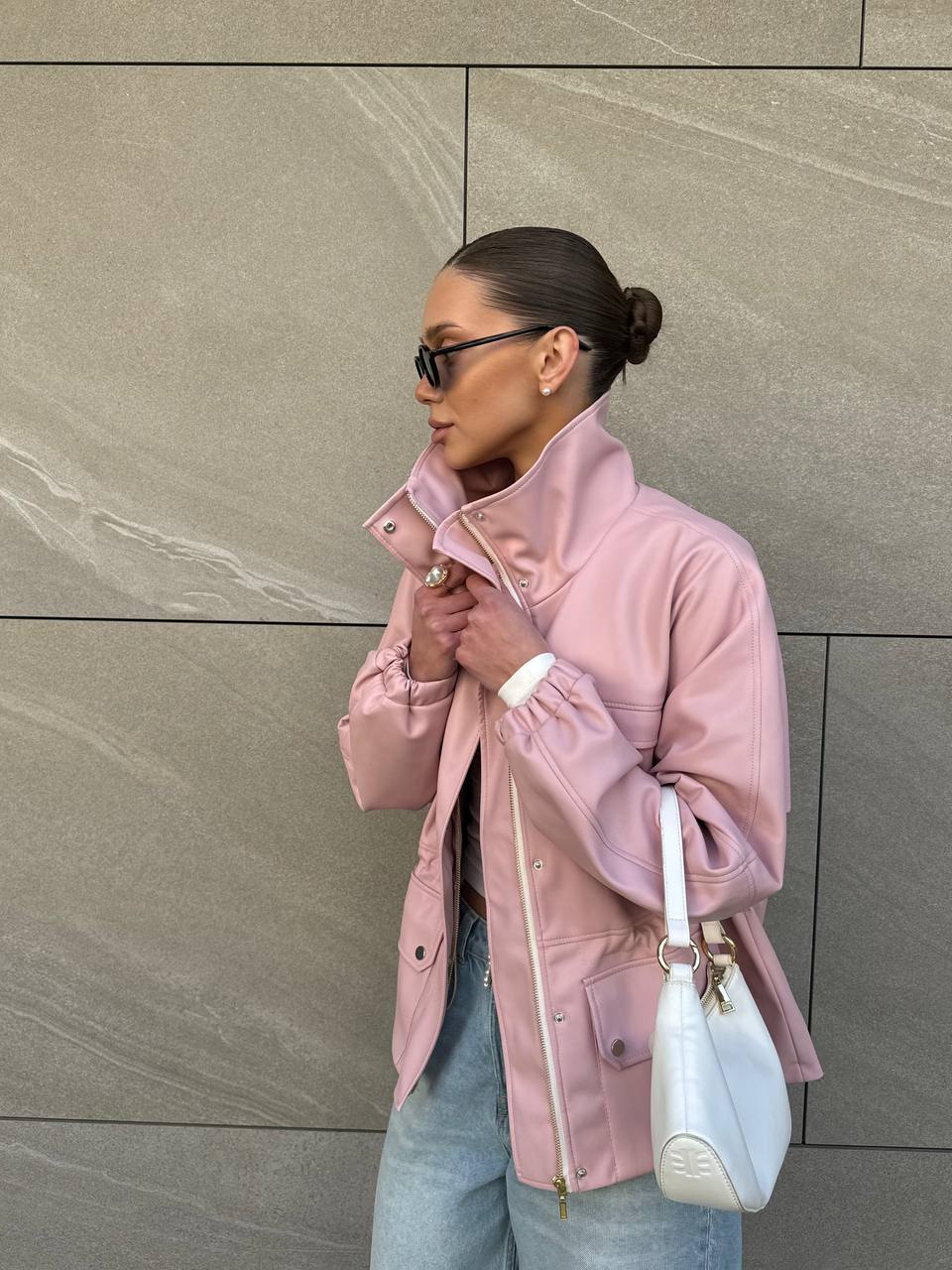 Woman wearing a pink coat and light blue jeans against a beige wall.
