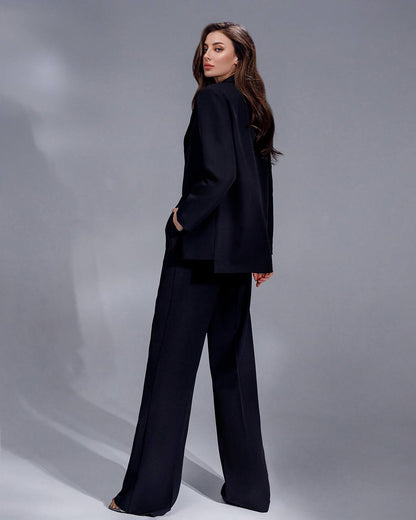 Woman wearing a black suit standing against a gray background