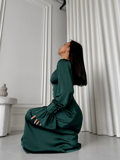 Woman in a green dress kneeling on a light-colored floor with white curtains in the background.