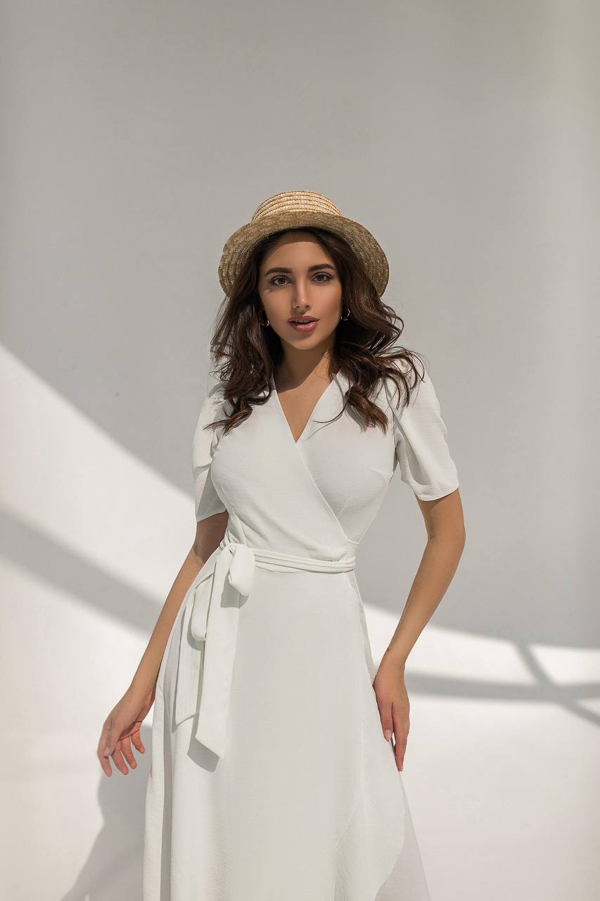 Woman wearing a white dress and straw hat against a plain background