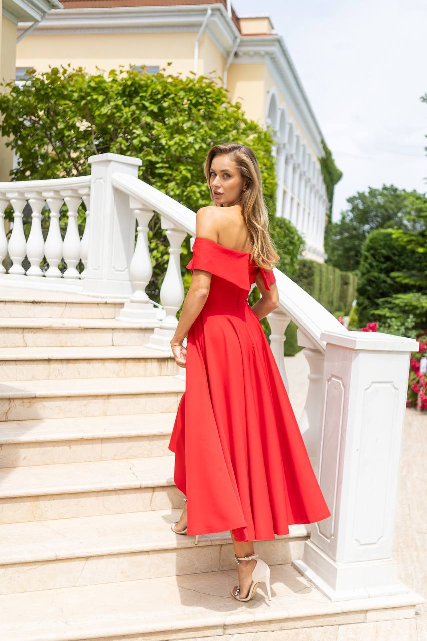 Woman in a red dress standing on a staircase with a white railing and greenery in the background.