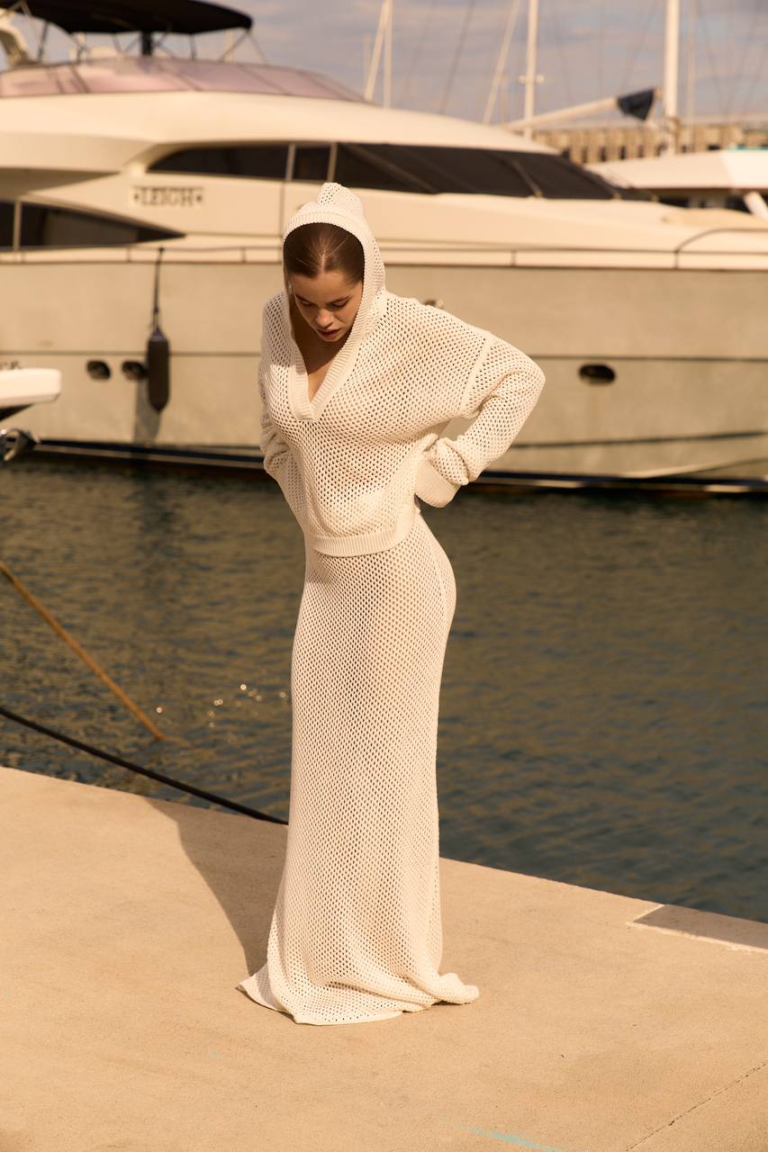 Woman in a white mesh outfit standing on a dock with yachts in the background