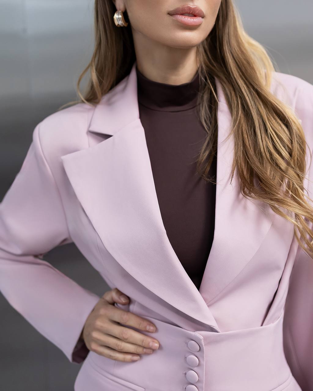 Woman wearing a light pink blazer over a dark top against a neutral background
