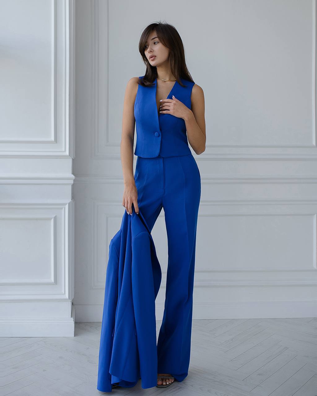 Woman wearing a blue jumpsuit against a white paneled wall.