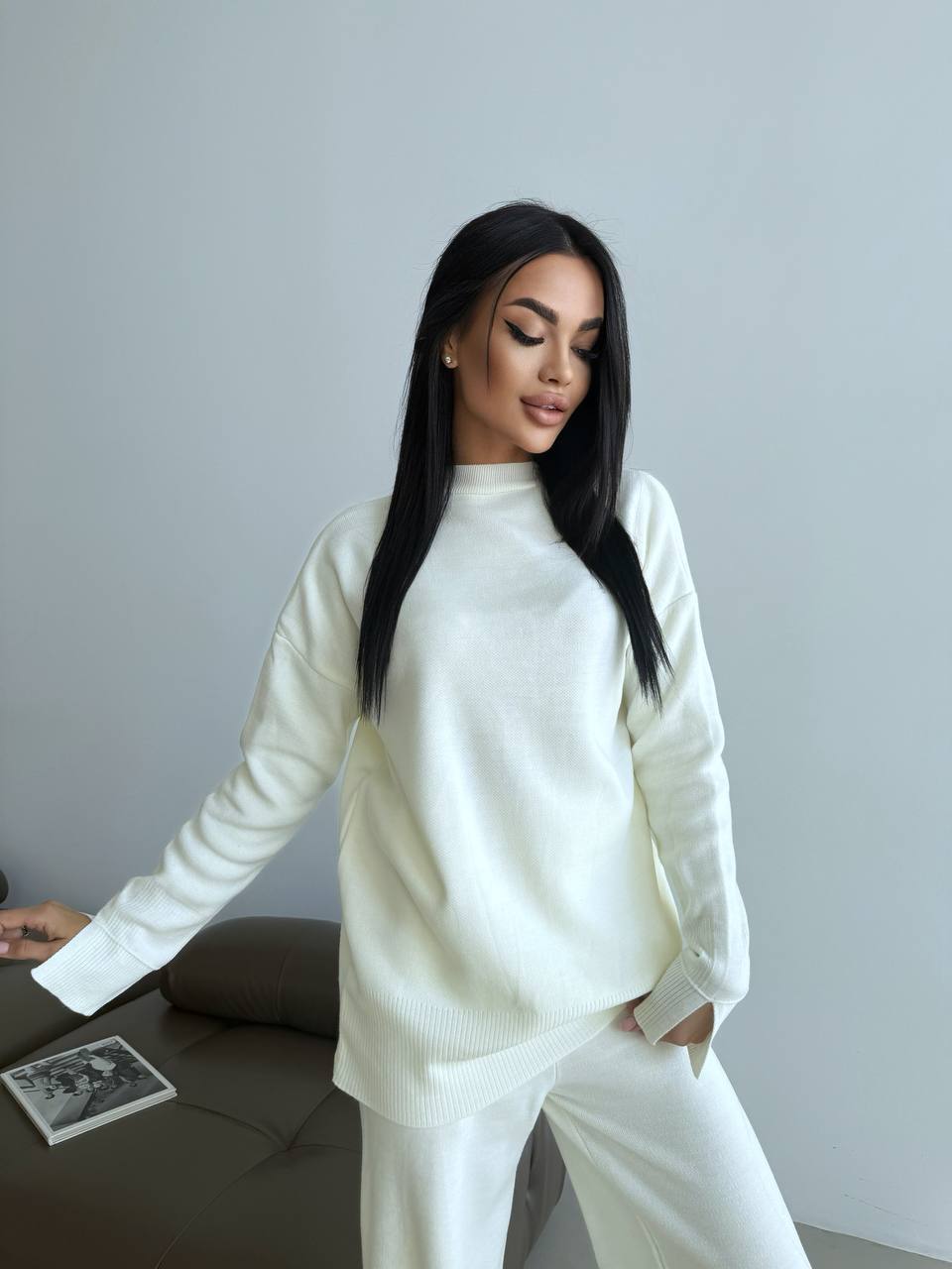 Woman in a white outfit sitting on a couch against a plain background