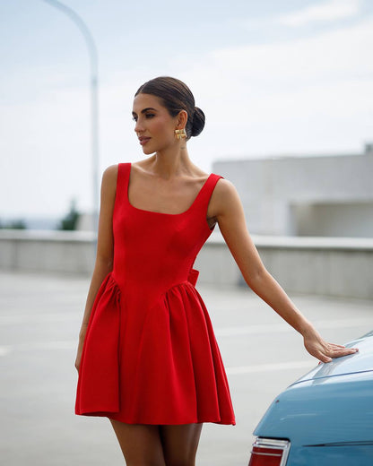 Woman in a red dress standing next to a blue car with a blurred background