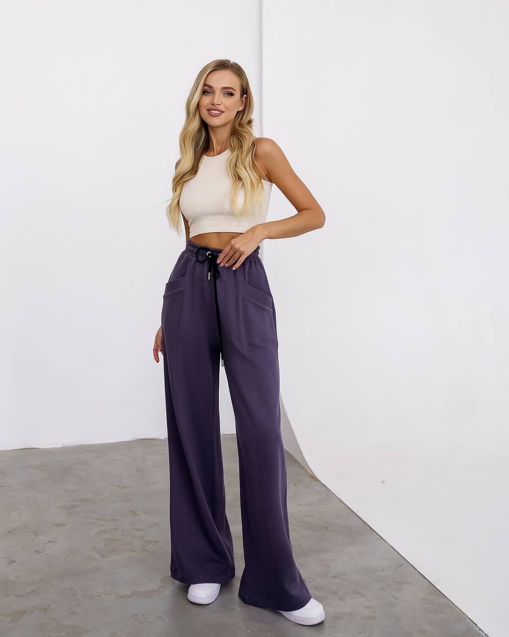 Woman wearing a white top and purple pants against a white background