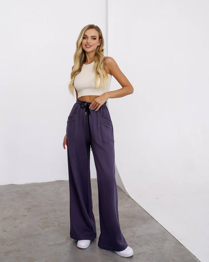 Woman wearing a white top and purple pants against a white background