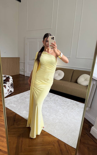 Woman in a yellow dress taking a mirror selfie in a room with a beige sofa and white walls.