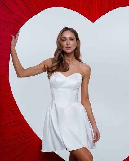 Woman in a white dress standing against a red heart-shaped backdrop