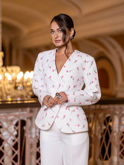Woman wearing a white blazer with pink floral patterns in an elegant indoor setting.