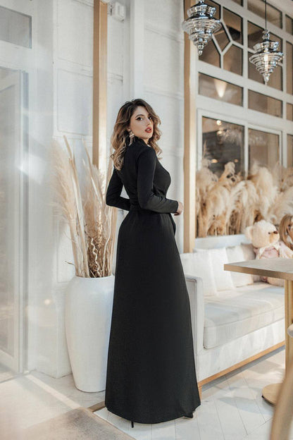 Woman in a black dress standing in a stylish interior setting with decor elements.