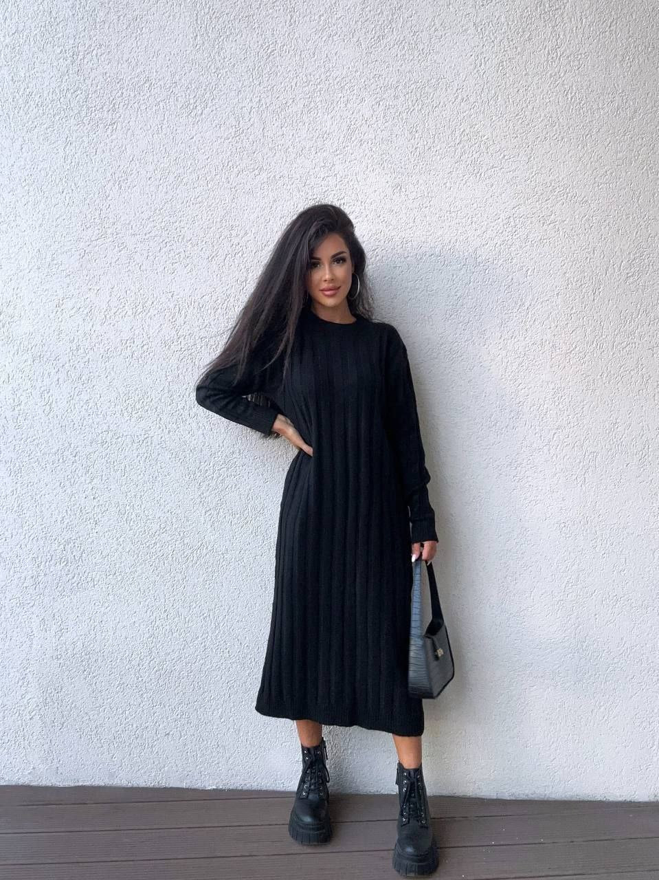 Person wearing a black dress standing against a white wall