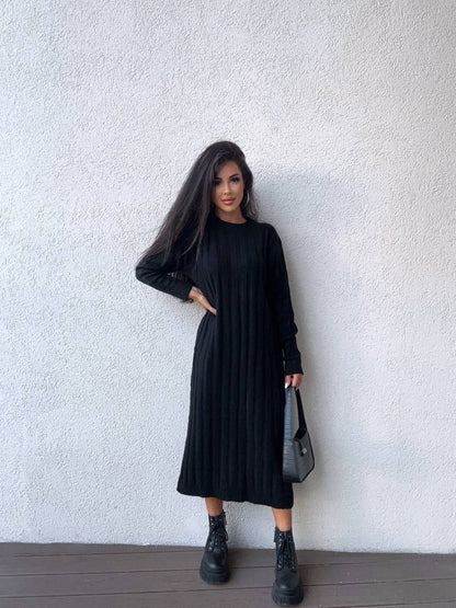 Person wearing a black dress standing against a white wall