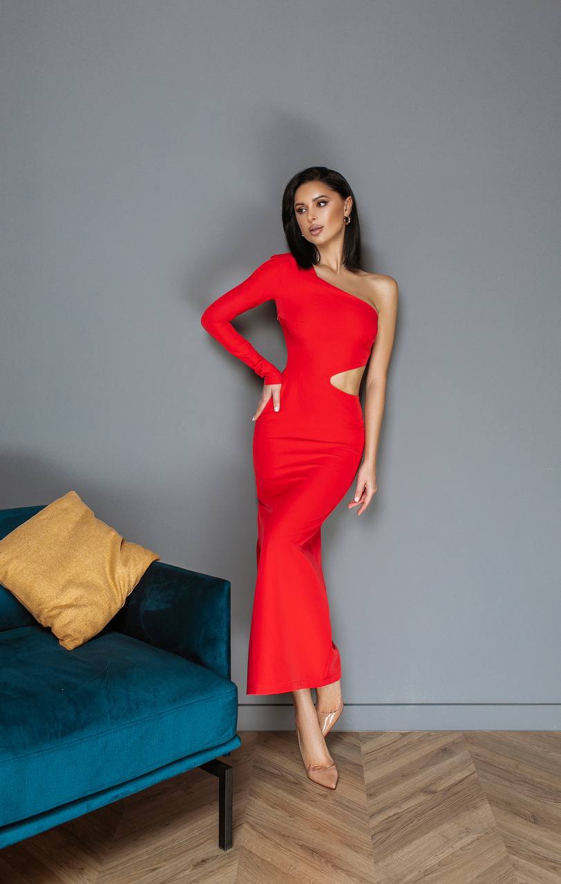 Woman in a red one-shoulder dress standing against a gray wall with a blue couch and yellow pillow.