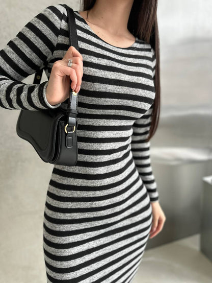 Person wearing a black and white striped dress holding a black handbag.