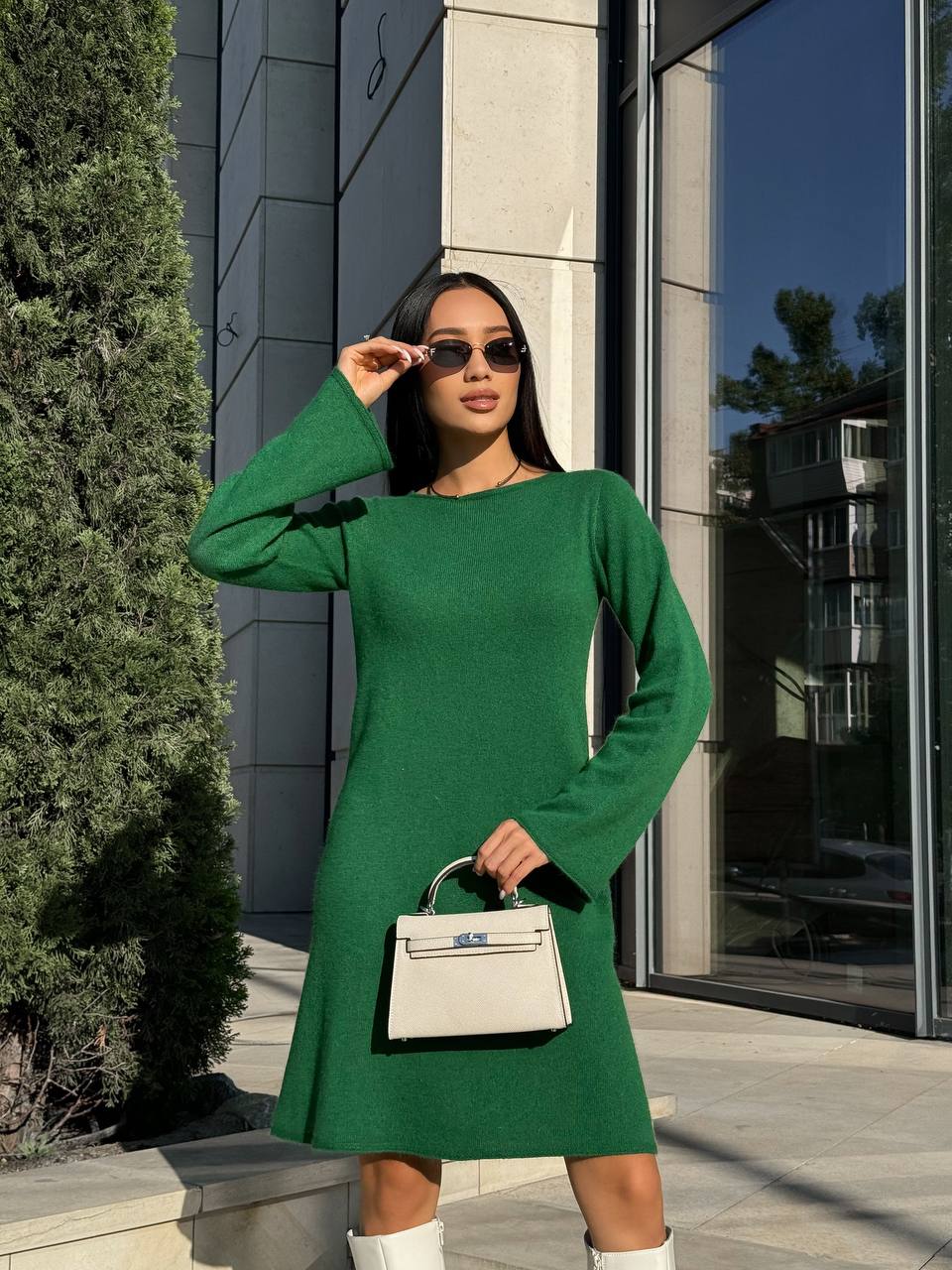 Woman in a green dress holding a white handbag outdoors.
