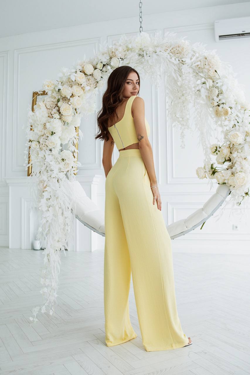 Woman in a yellow jumpsuit standing in front of a floral arch